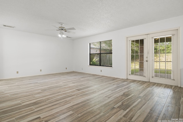 empty room featuring ceiling fan, light hardwood / wood-style floors, french doors, and plenty of natural light