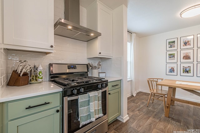 kitchen with stainless steel range with gas stovetop, wall chimney exhaust hood, green cabinetry, backsplash, and dark wood-type flooring