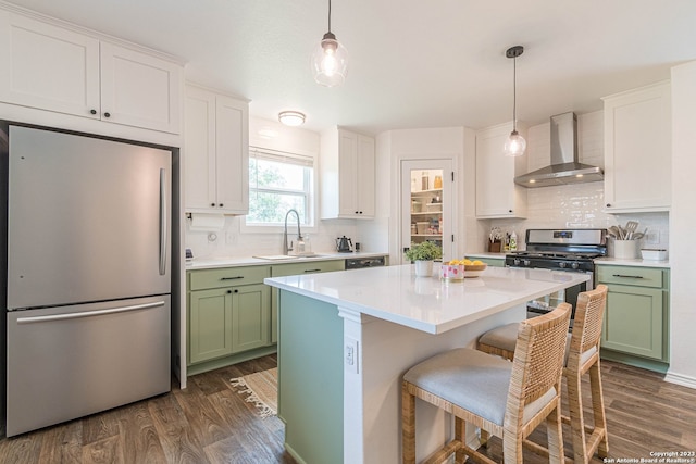 kitchen with wall chimney range hood, dark wood-type flooring, stainless steel appliances, and green cabinetry