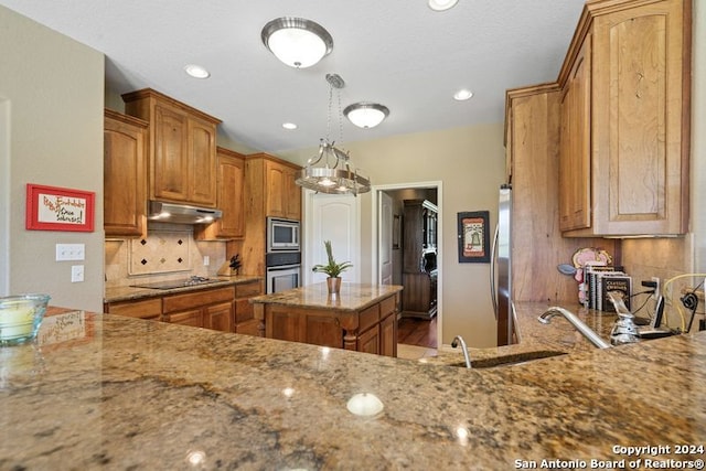 kitchen featuring sink, tasteful backsplash, light stone counters, a center island, and appliances with stainless steel finishes