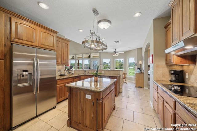 kitchen with pendant lighting, a kitchen island, light stone countertops, and stainless steel built in refrigerator