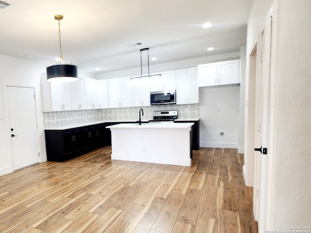 kitchen with electric range oven, hanging light fixtures, light hardwood / wood-style floors, decorative backsplash, and an island with sink