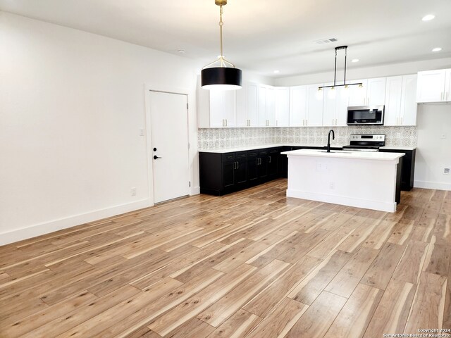 kitchen with appliances with stainless steel finishes, light hardwood / wood-style flooring, pendant lighting, and a kitchen island with sink