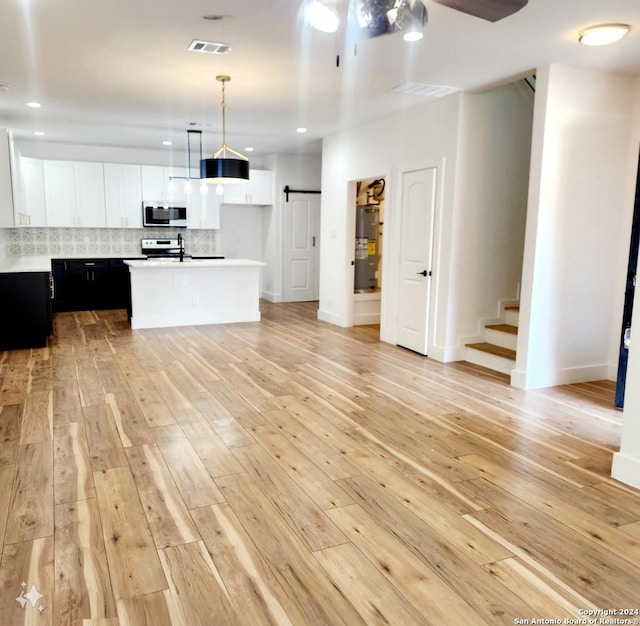 kitchen with an island with sink, white cabinetry, light wood-type flooring, a barn door, and decorative light fixtures