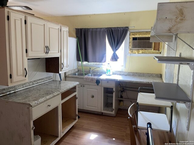 kitchen featuring a wall mounted AC, a sink, light stone countertops, wood finished floors, and white cabinets