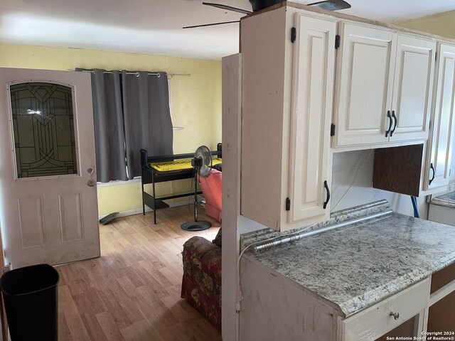 kitchen with baseboards, white cabinetry, light wood-style flooring, and light stone countertops