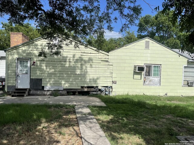 exterior space featuring a lawn, a chimney, a wall mounted AC, and entry steps