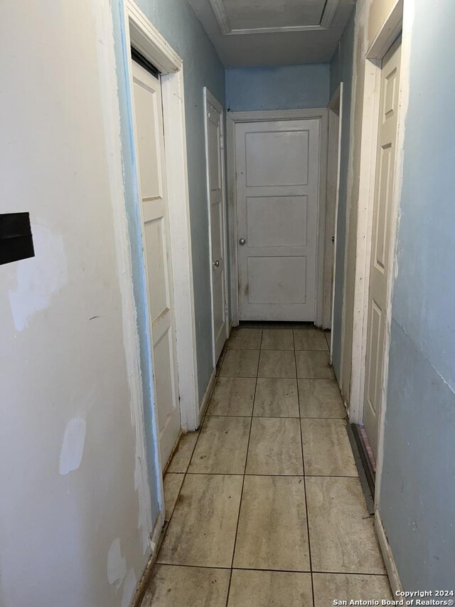hall featuring light tile patterned floors and attic access