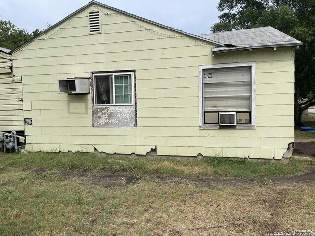 view of home's exterior featuring cooling unit, a wall mounted AC, and roof with shingles