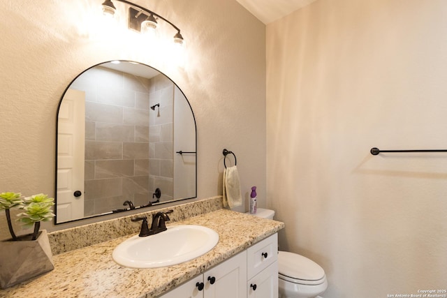 full bath with toilet, a textured wall, and vanity