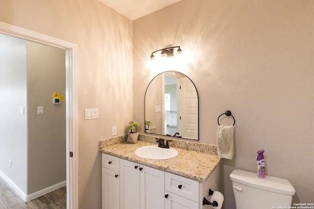 half bathroom featuring baseboards, vanity, toilet, and wood finished floors