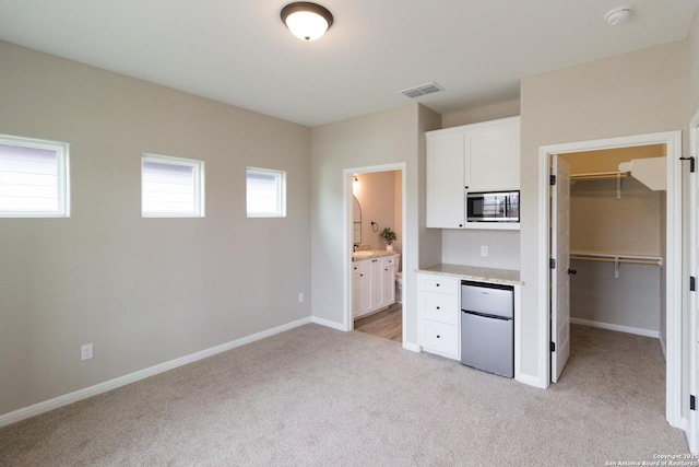 unfurnished bedroom with light carpet, baseboards, visible vents, a spacious closet, and fridge