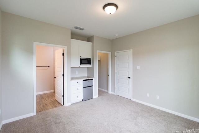 unfurnished bedroom with baseboards, refrigerator, visible vents, and light colored carpet