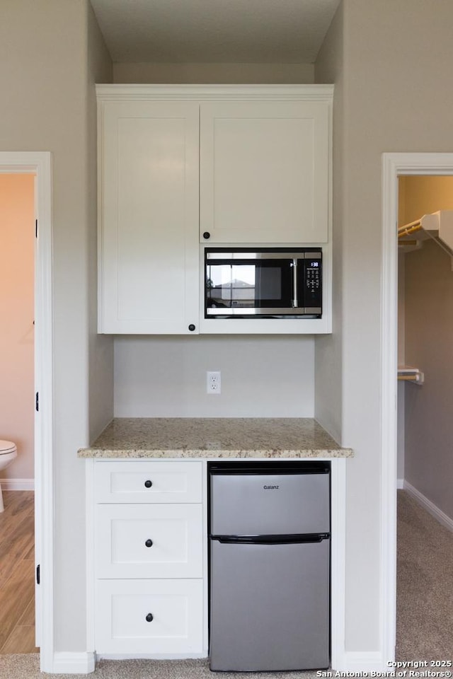 kitchen featuring light stone counters, appliances with stainless steel finishes, white cabinets, light carpet, and baseboards