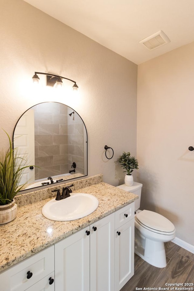 bathroom featuring baseboards, visible vents, toilet, wood finished floors, and vanity