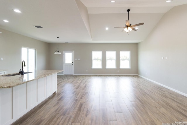 kitchen featuring open floor plan, a sink, white cabinets, and light stone countertops