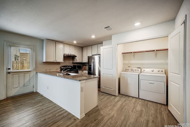 kitchen featuring dark stone counters, light wood-type flooring, sink, separate washer and dryer, and kitchen peninsula