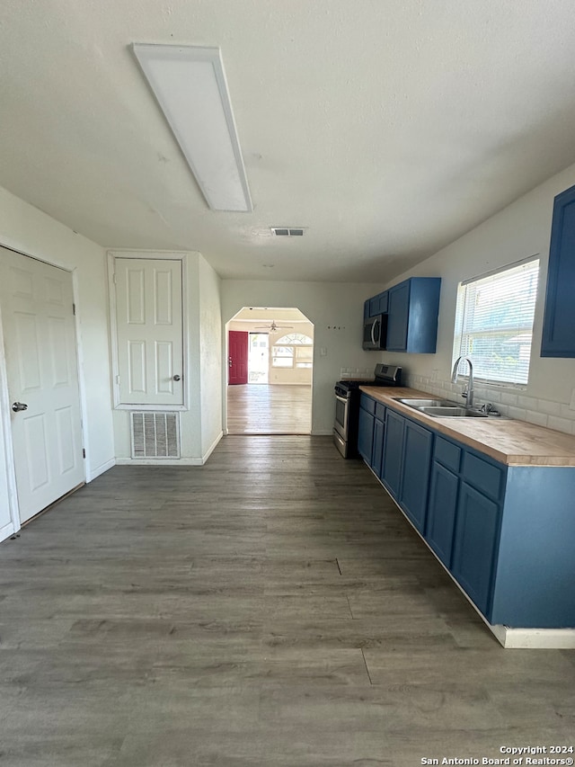 kitchen with appliances with stainless steel finishes, wood counters, hardwood / wood-style floors, sink, and blue cabinets