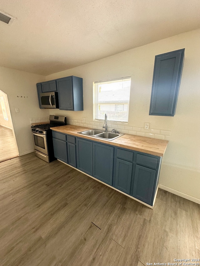 kitchen with hardwood / wood-style flooring, wood counters, appliances with stainless steel finishes, and sink