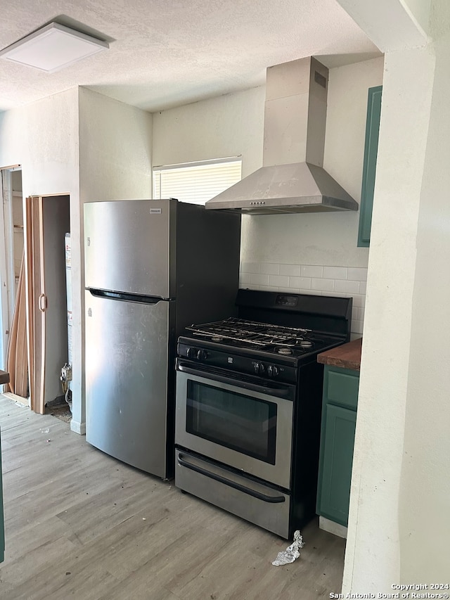 kitchen featuring wall chimney exhaust hood, light hardwood / wood-style floors, a textured ceiling, appliances with stainless steel finishes, and green cabinetry