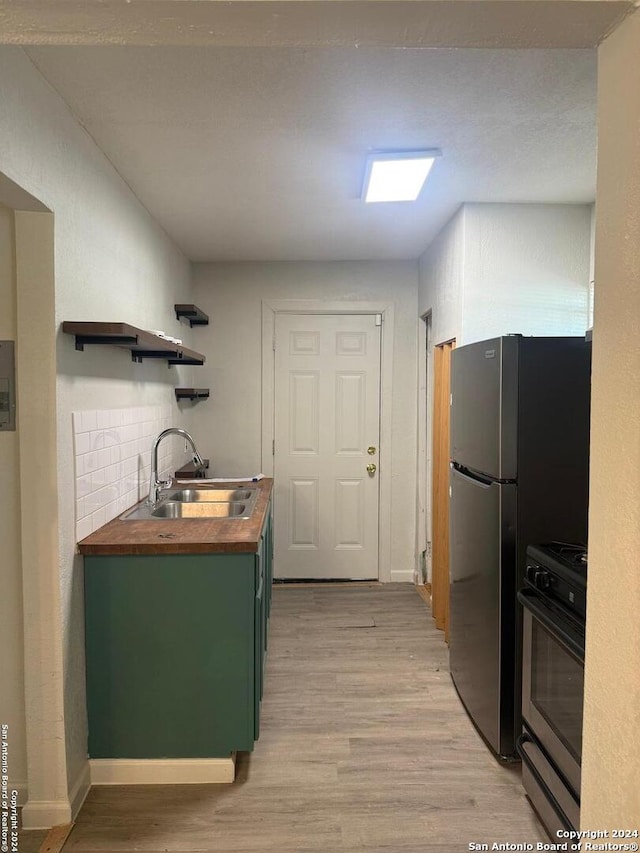 kitchen featuring wood counters, black range, green cabinets, sink, and light hardwood / wood-style flooring