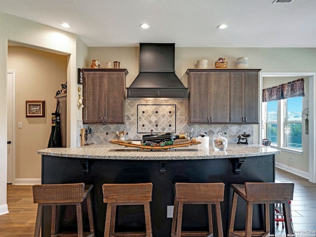 kitchen featuring light stone counters, premium range hood, wood-type flooring, and dark brown cabinetry