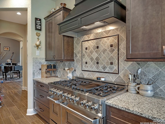 kitchen featuring stainless steel range, tasteful backsplash, custom range hood, and light stone countertops