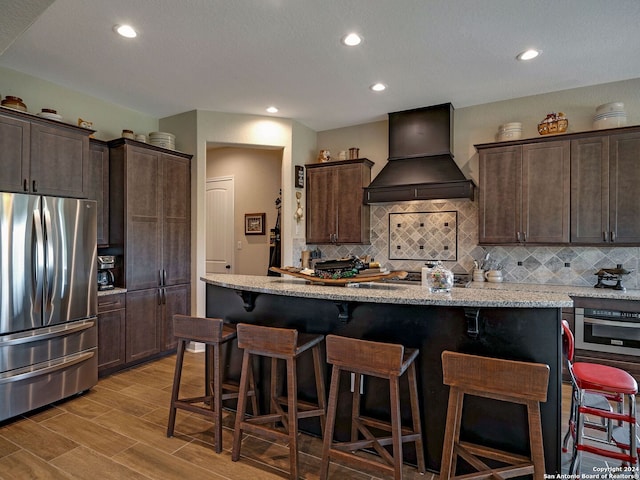 kitchen with stainless steel appliances, decorative backsplash, light wood-type flooring, a kitchen island, and custom exhaust hood