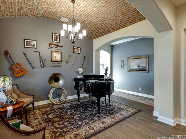 sitting room with an inviting chandelier, hardwood / wood-style floors, lofted ceiling, and brick ceiling