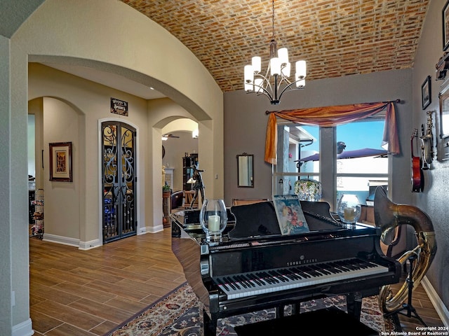 miscellaneous room featuring a notable chandelier, hardwood / wood-style floors, vaulted ceiling, and brick ceiling