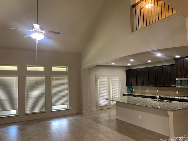 kitchen featuring ceiling fan, high vaulted ceiling, sink, light stone countertops, and a center island with sink