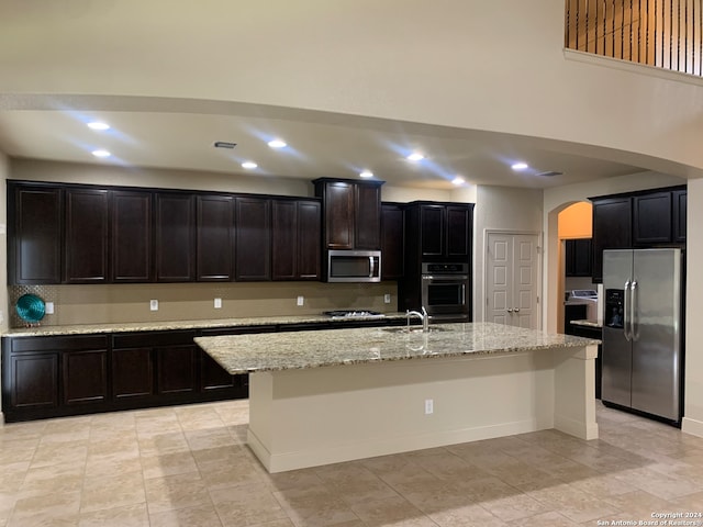 kitchen featuring a center island with sink, stainless steel appliances, light stone countertops, and light tile patterned floors