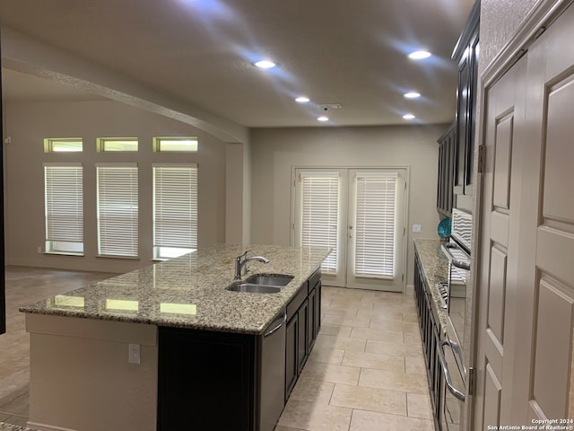 kitchen featuring light tile patterned flooring, dishwasher, an island with sink, light stone countertops, and sink