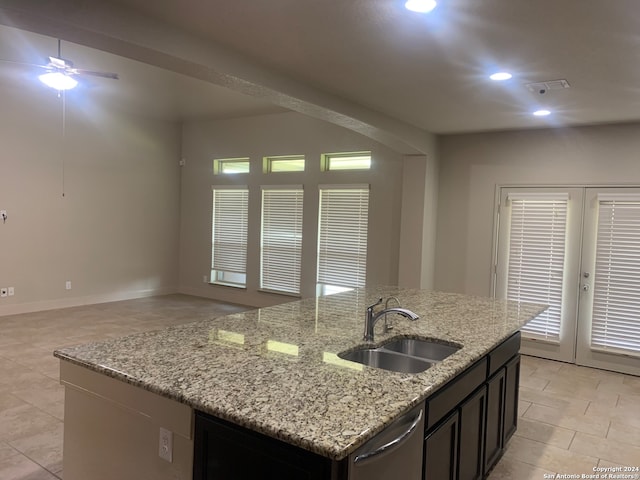 kitchen with sink, light stone counters, an island with sink, dishwasher, and ceiling fan