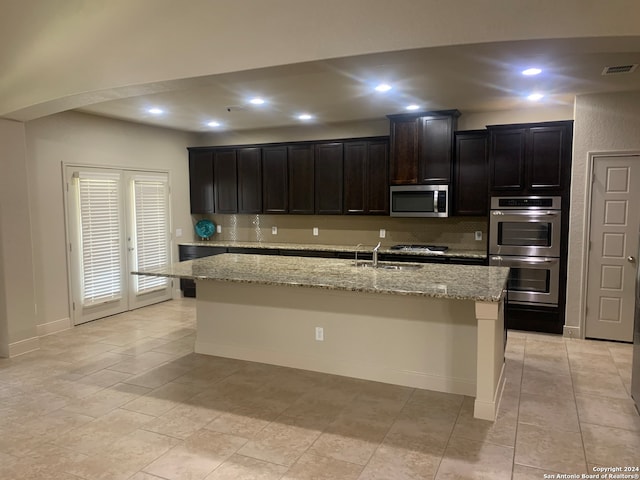 kitchen with stainless steel appliances, sink, light stone countertops, light tile patterned floors, and a kitchen island with sink