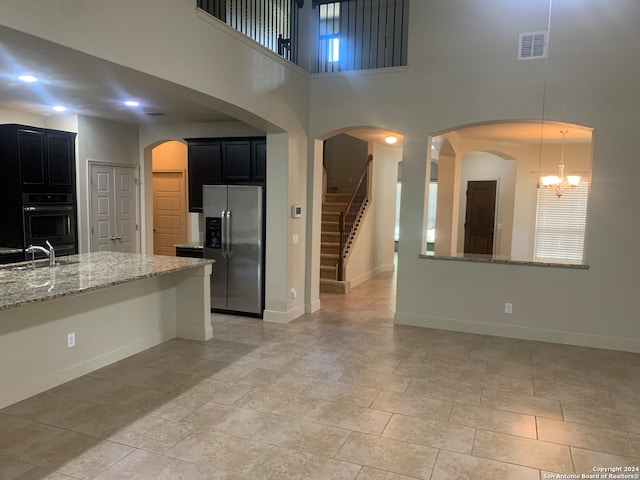 kitchen with stainless steel fridge with ice dispenser, sink, an inviting chandelier, light stone countertops, and a towering ceiling