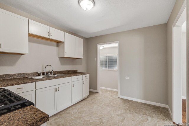 kitchen with light tile patterned flooring, sink, gas stovetop, and white cabinets