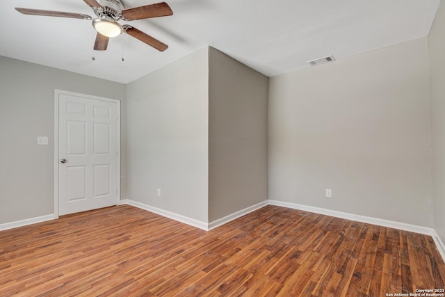 spare room with a ceiling fan, visible vents, baseboards, and wood finished floors