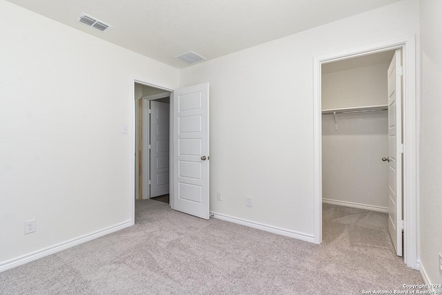 unfurnished bedroom with a walk in closet, a closet, and light carpet