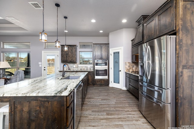 kitchen featuring a large island, sink, stainless steel appliances, dark brown cabinetry, and decorative light fixtures