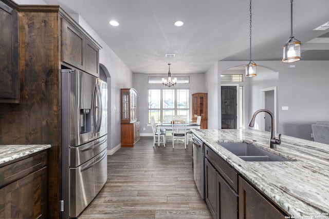 kitchen with wood-type flooring, sink, stainless steel appliances, light stone countertops, and dark brown cabinets