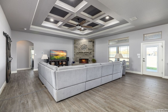 living room with crown molding, coffered ceiling, wood-type flooring, a stone fireplace, and beamed ceiling