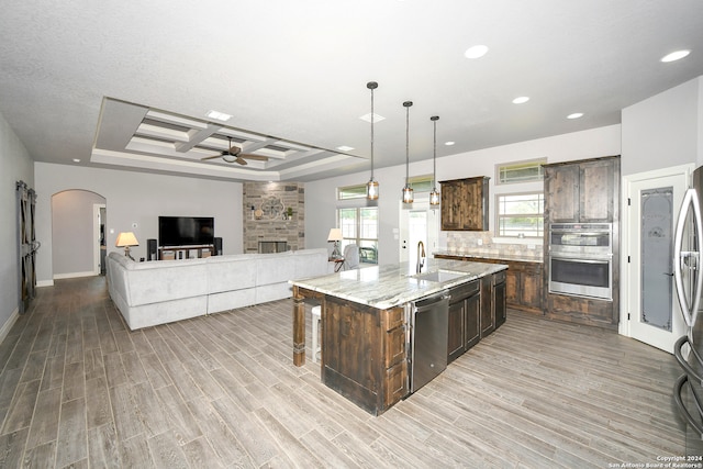 kitchen with sink, stainless steel appliances, light stone counters, decorative light fixtures, and a kitchen island with sink