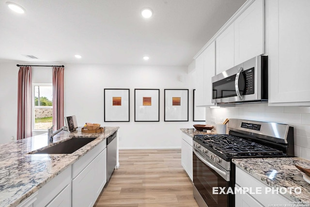 kitchen with light stone counters, sink, white cabinetry, light hardwood / wood-style flooring, and appliances with stainless steel finishes