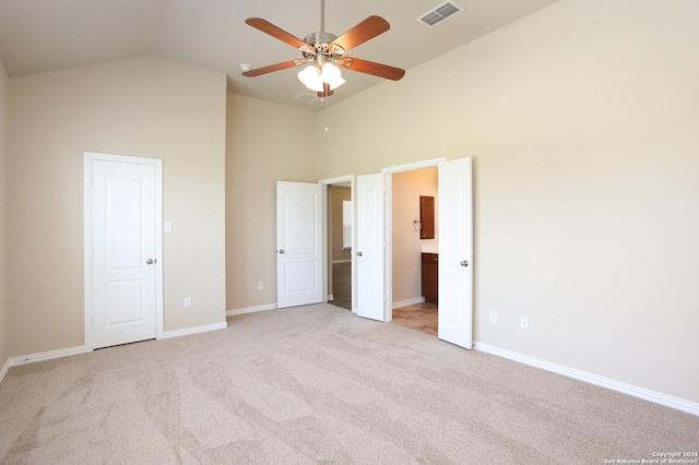 unfurnished bedroom featuring ceiling fan, light colored carpet, ensuite bathroom, and high vaulted ceiling