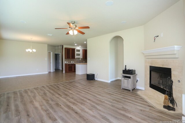 unfurnished living room featuring a fireplace, light wood-type flooring, and ceiling fan with notable chandelier