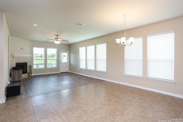 unfurnished living room with ceiling fan with notable chandelier, a fireplace, and light tile patterned floors