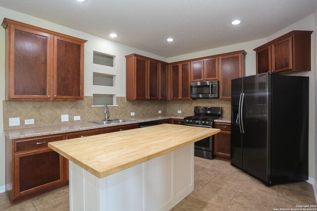 kitchen with butcher block countertops, tasteful backsplash, black appliances, sink, and a center island