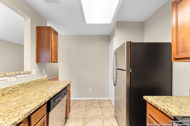 kitchen featuring light tile patterned flooring, appliances with stainless steel finishes, light stone counters, and a skylight