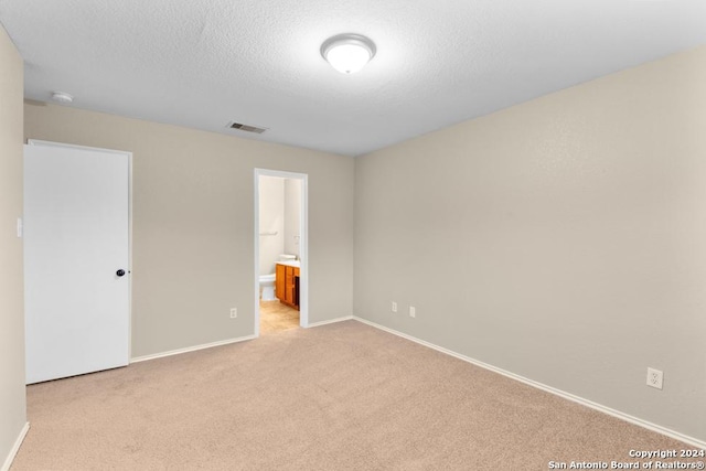 unfurnished bedroom featuring ensuite bathroom, a textured ceiling, and light colored carpet